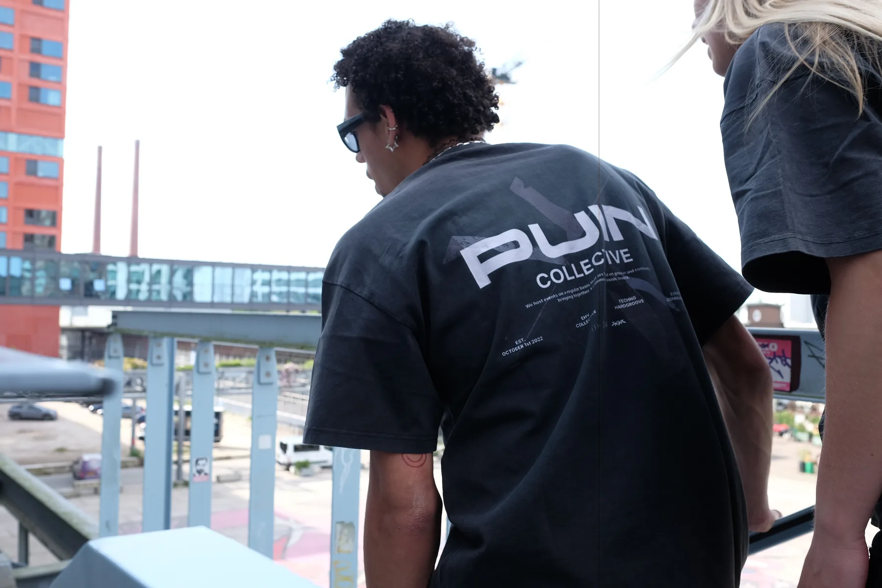 Back of a Puin Collective t-shirt in an industrial urban setting