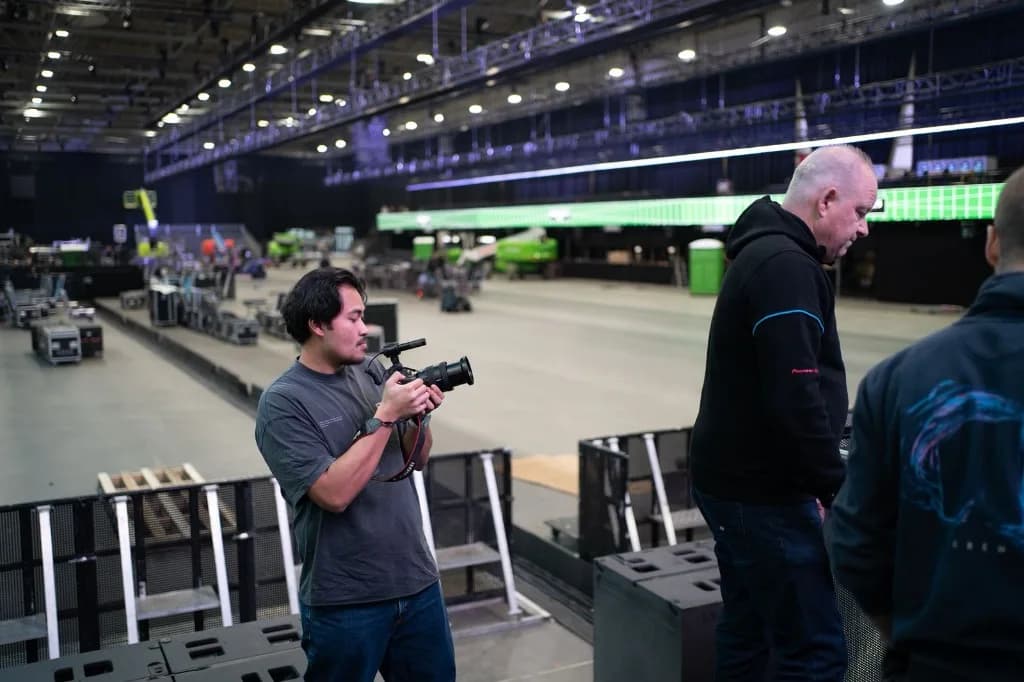 Camera operator reviewing settings on an arena floor during event production load-in