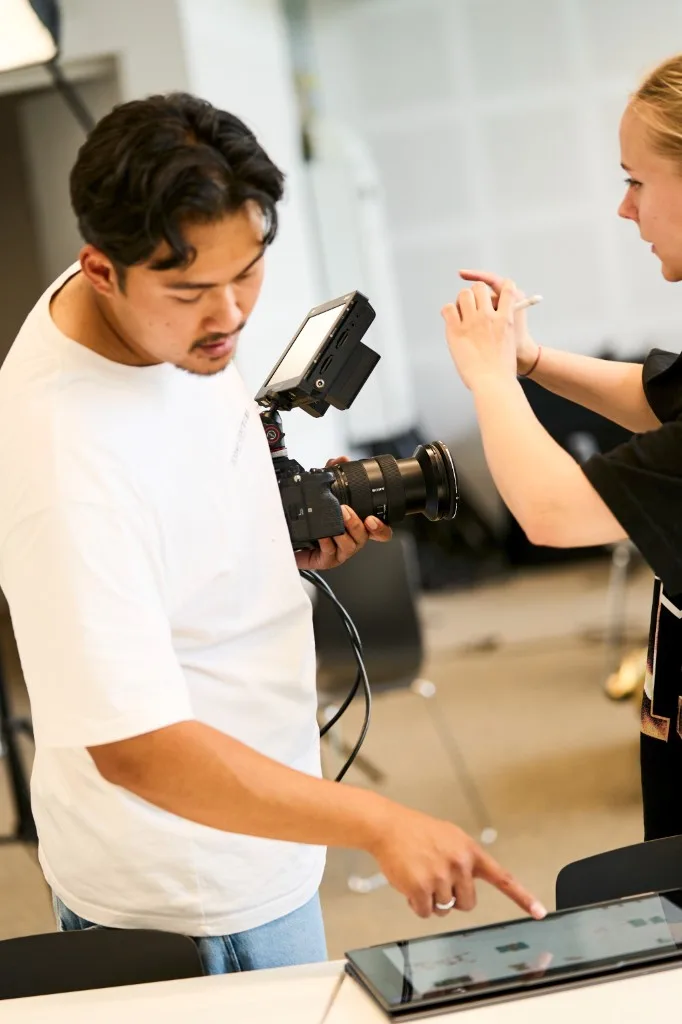 Adryan reviewing footage on a tablet while holding a professional camera during a studio production