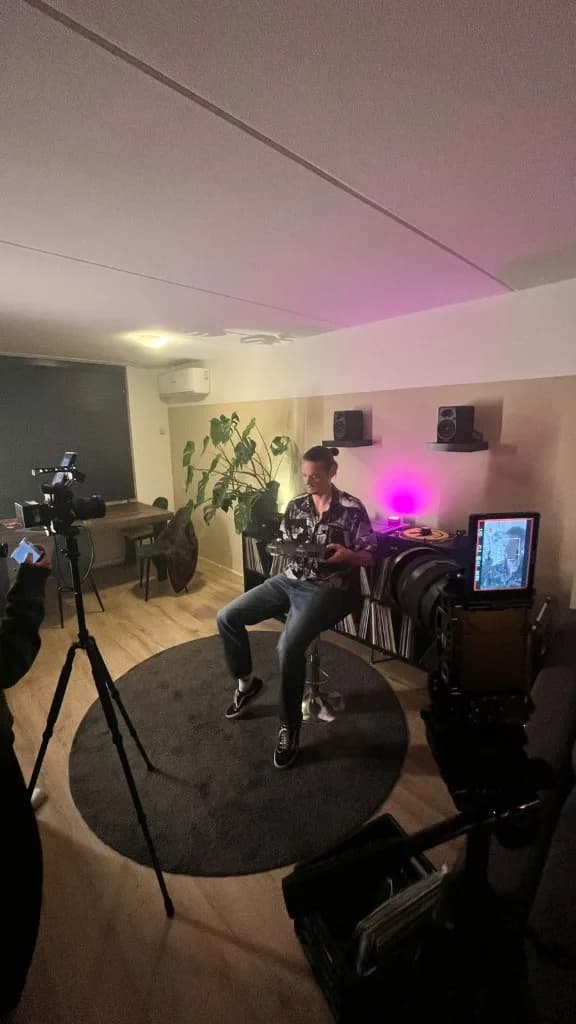 Dual-camera studio setup filming a subject seated among vinyl records with magenta accent lighting
