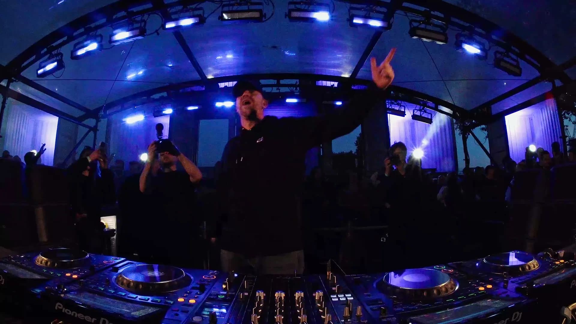 Low booth angle on the DJ mid-set under blue stage lights