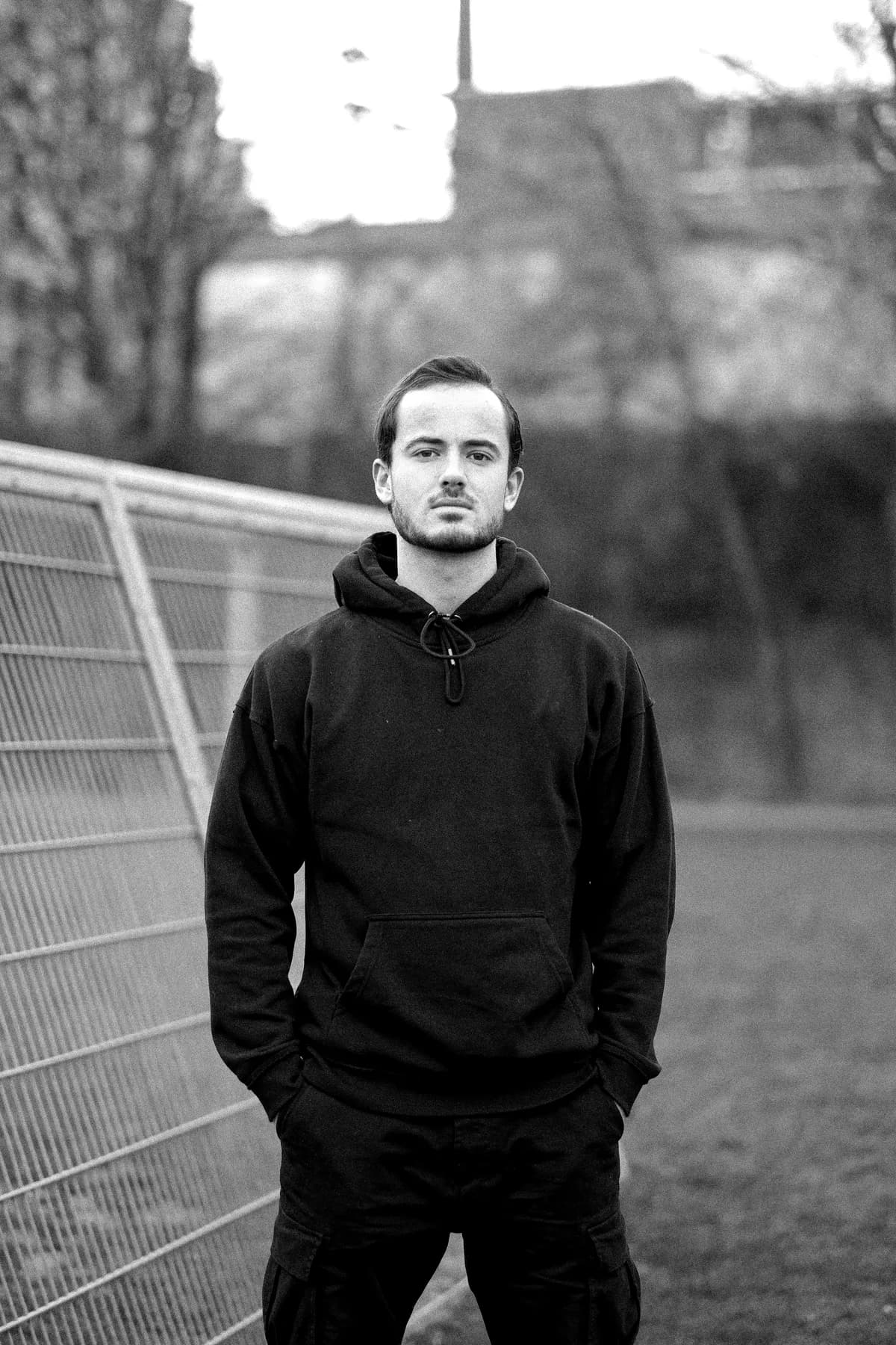 Black-and-white press portrait of a man in a hoodie against a soft outdoor backdrop